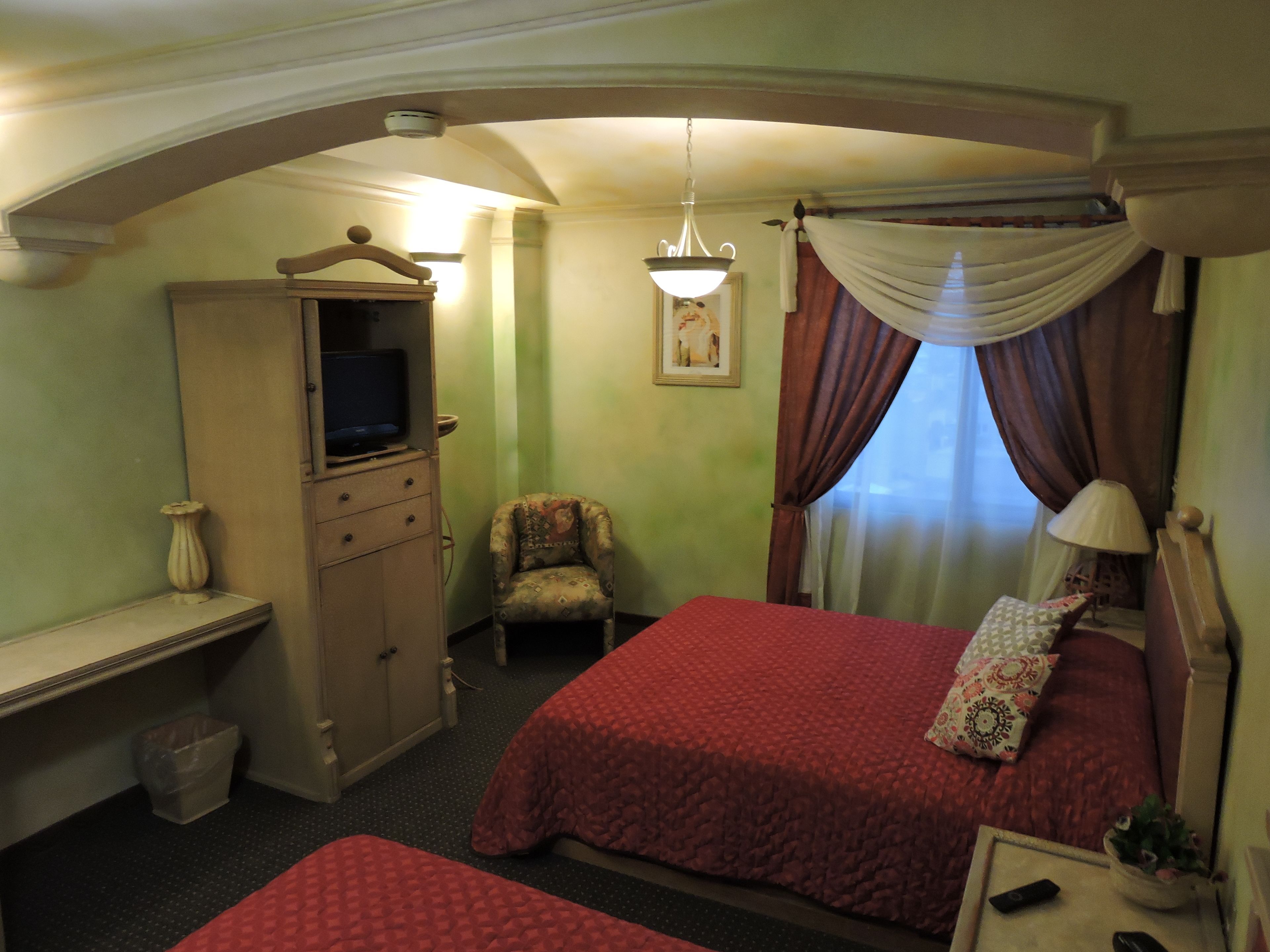 A hotel room with two beds, a television on a cabinet, a chair, a desk, and a lamp.