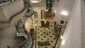 A hotel lobby with a checkered floor, a staircase with green railings, and several seating areas.