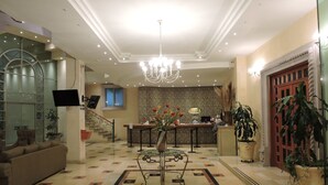 A lobby with a reception desk, a chandelier, a sofa, and potted plants.