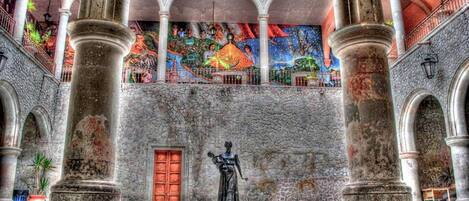 Un patio con una estatua, columnas de piedra y un mural colorido.