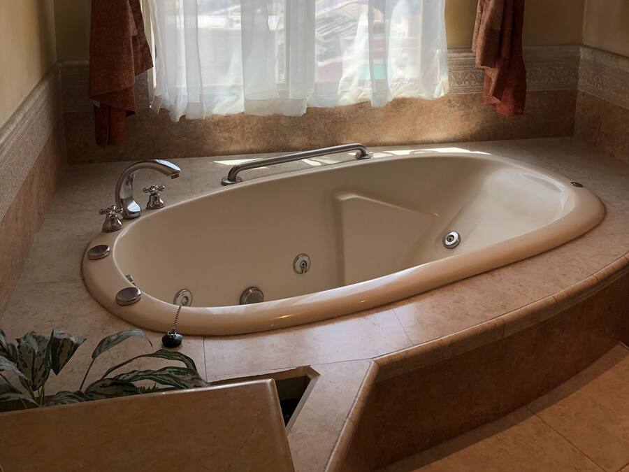 A bathroom with a large bathtub, a window with sheer curtains, and a view of the cityscape.