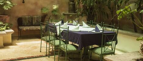 A dining area with tables set for four, surrounded by green chairs and a bench.