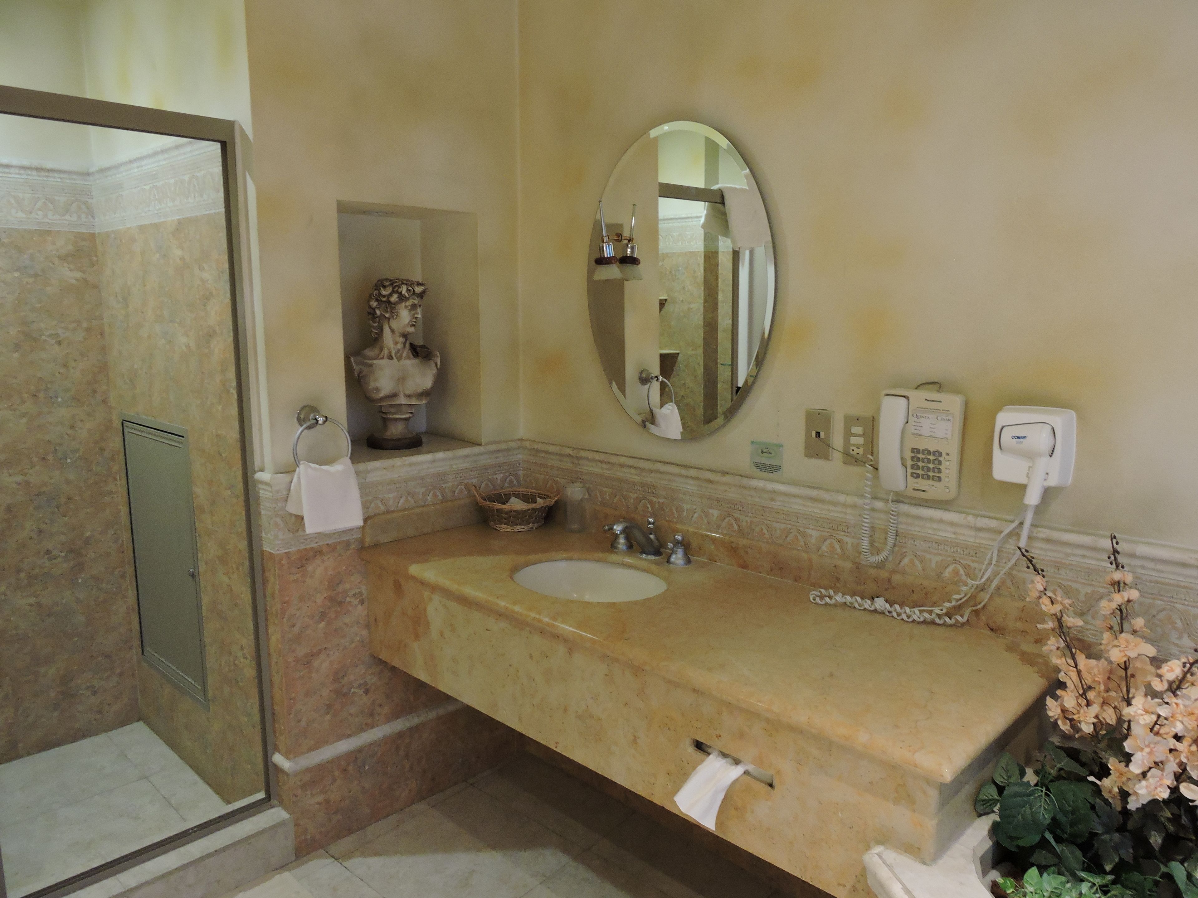 Une salle de bain avec un lavabo en marbre, un miroir, un téléphone et un espace douche.