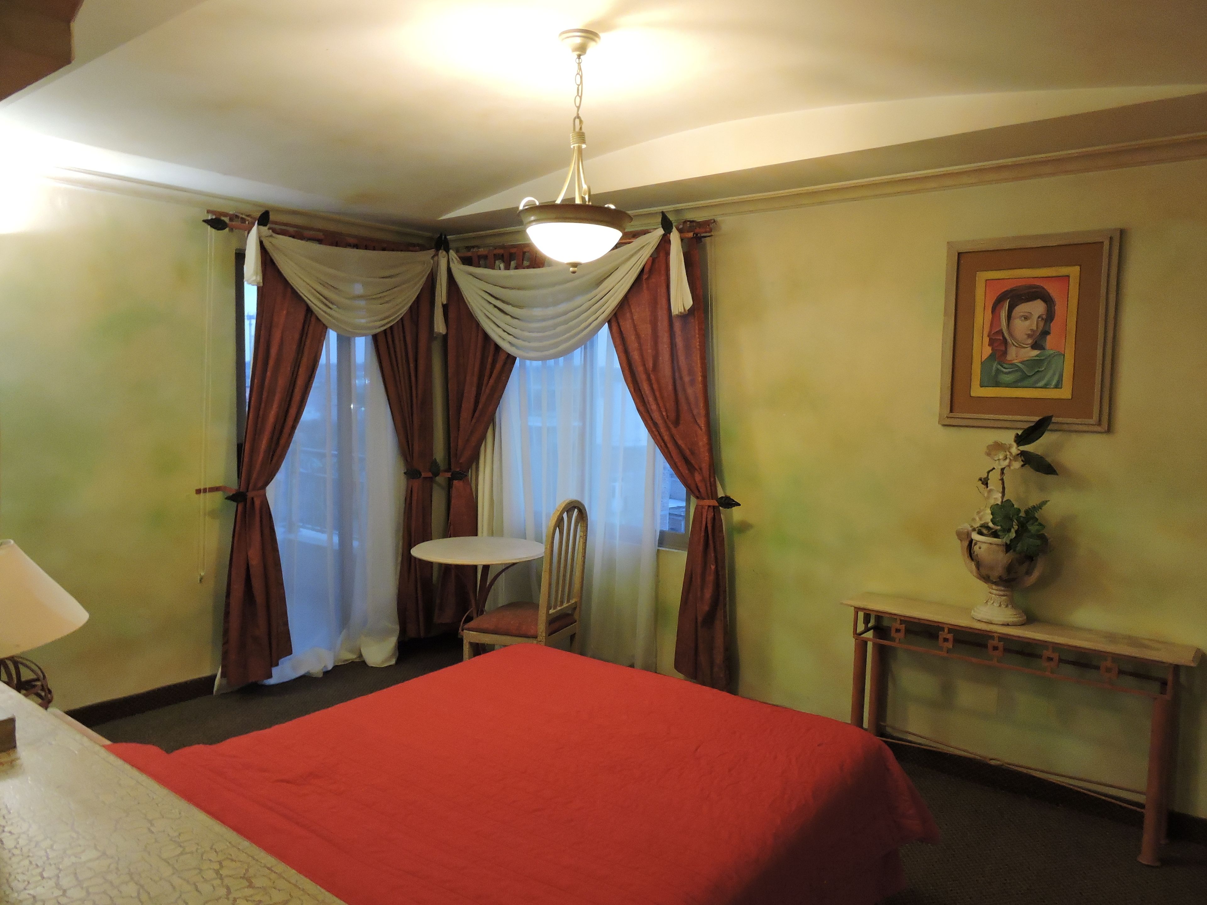 Een hotelkamer met een bed, een stoel, een tafeltje, een lamp en een schilderij aan de muur.