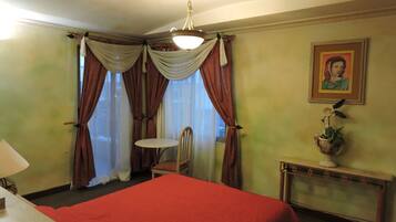 Een hotelkamer met een bed, een stoel, een tafeltje, een lamp en een schilderij aan de muur.
