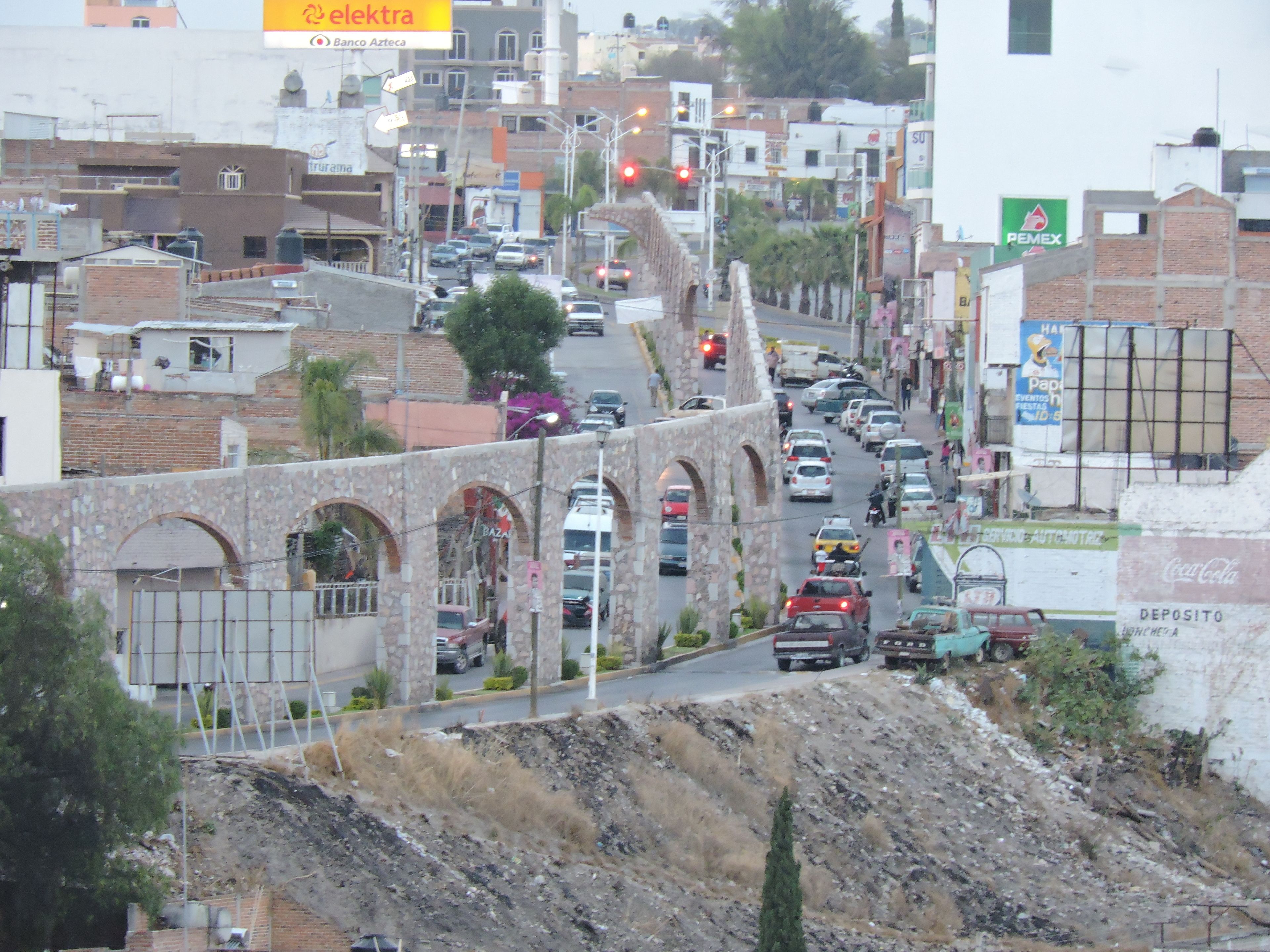 Una concurrida calle urbana con arcos de piedra, automóviles y diversos edificios comerciales.