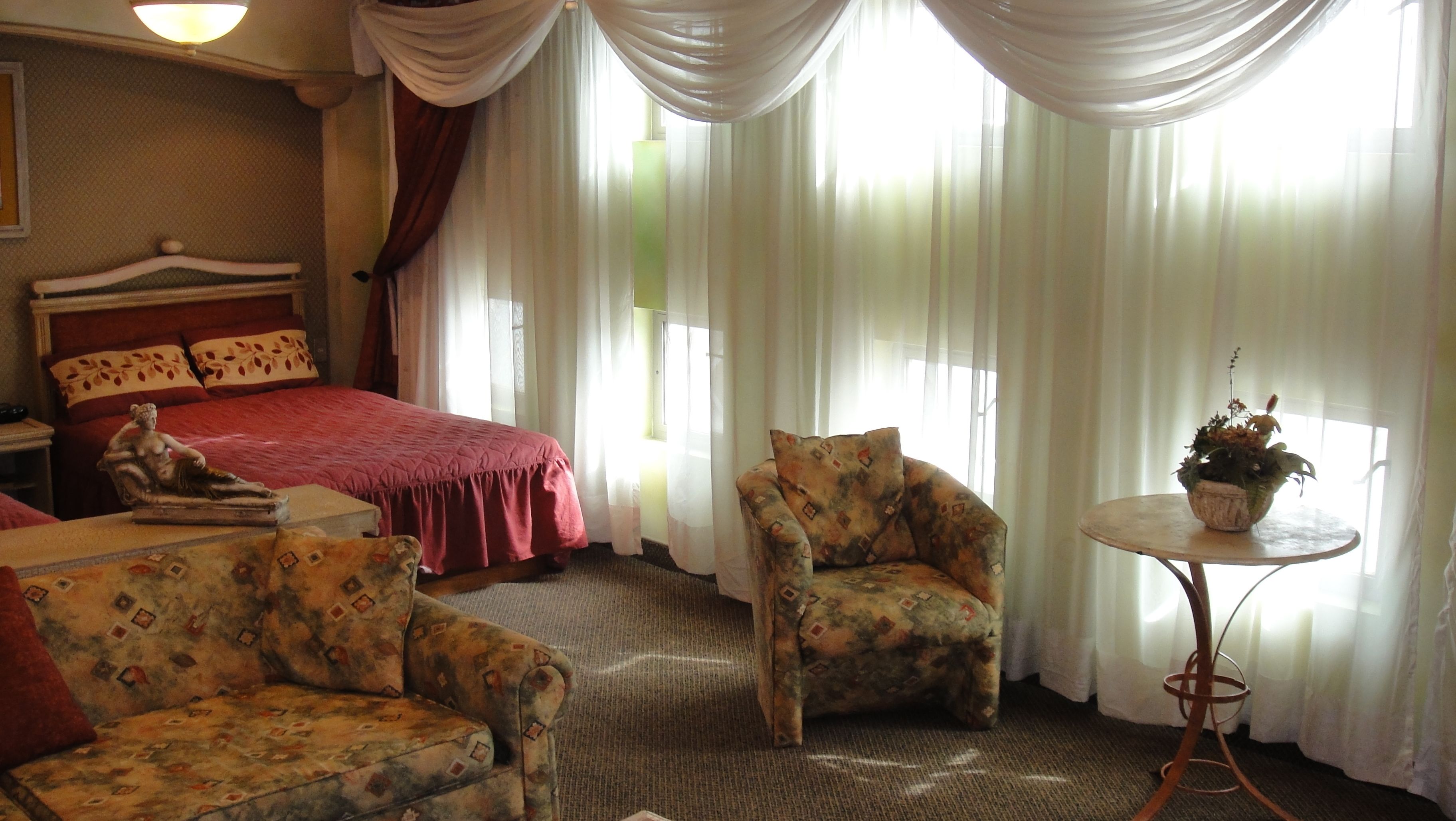 Una habitación de hotel con una cama, dos sillones, una mesita con una planta y una estatua.