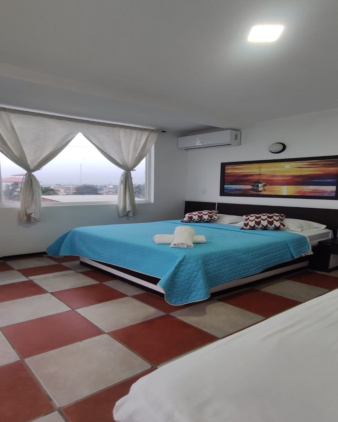 A hotel room with a bed, a nightstand, a painting, and a window with curtains.