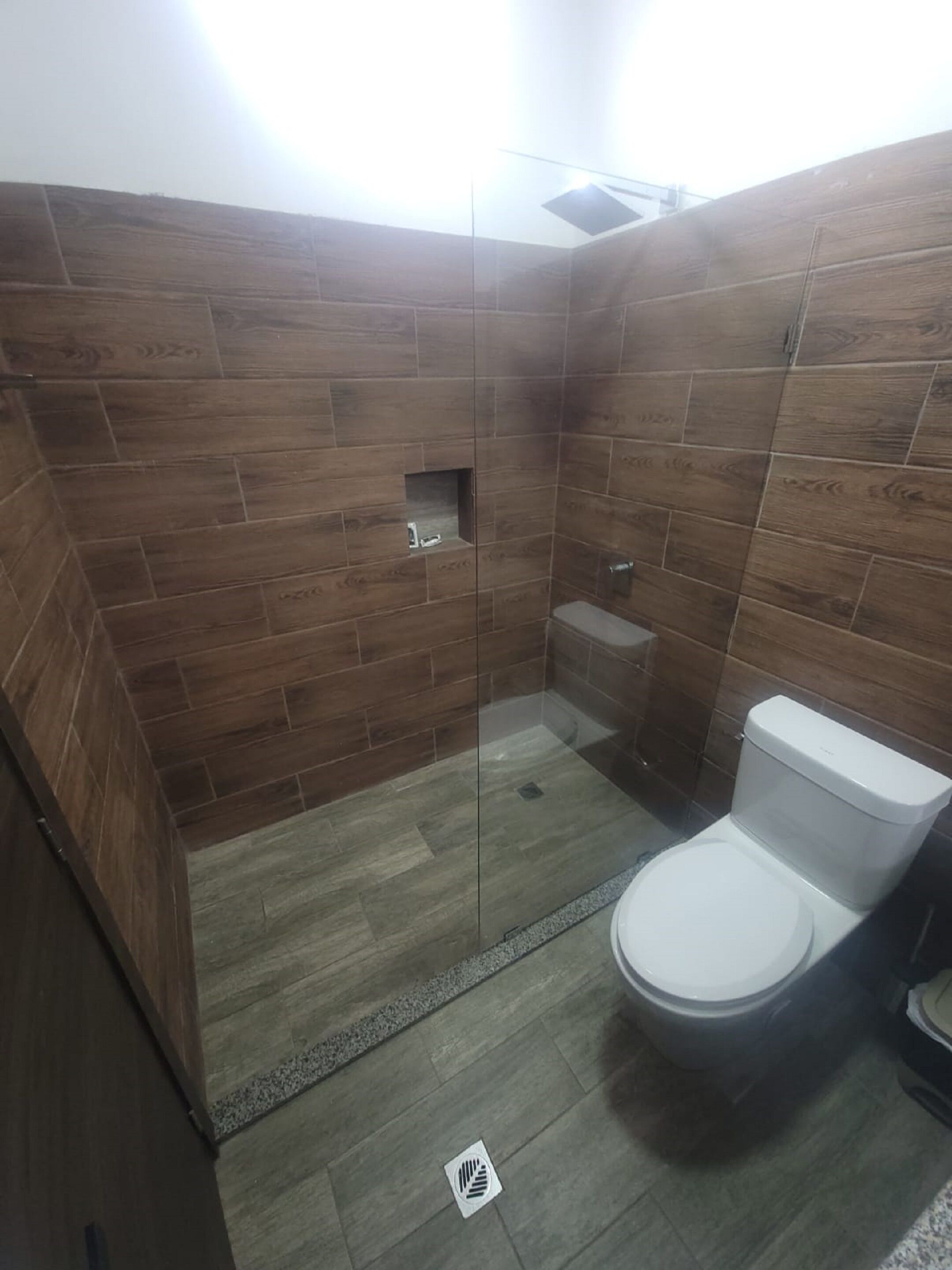Baño con paredes de madera, cabina de ducha con mampara de vidrio y un inodoro blanco.