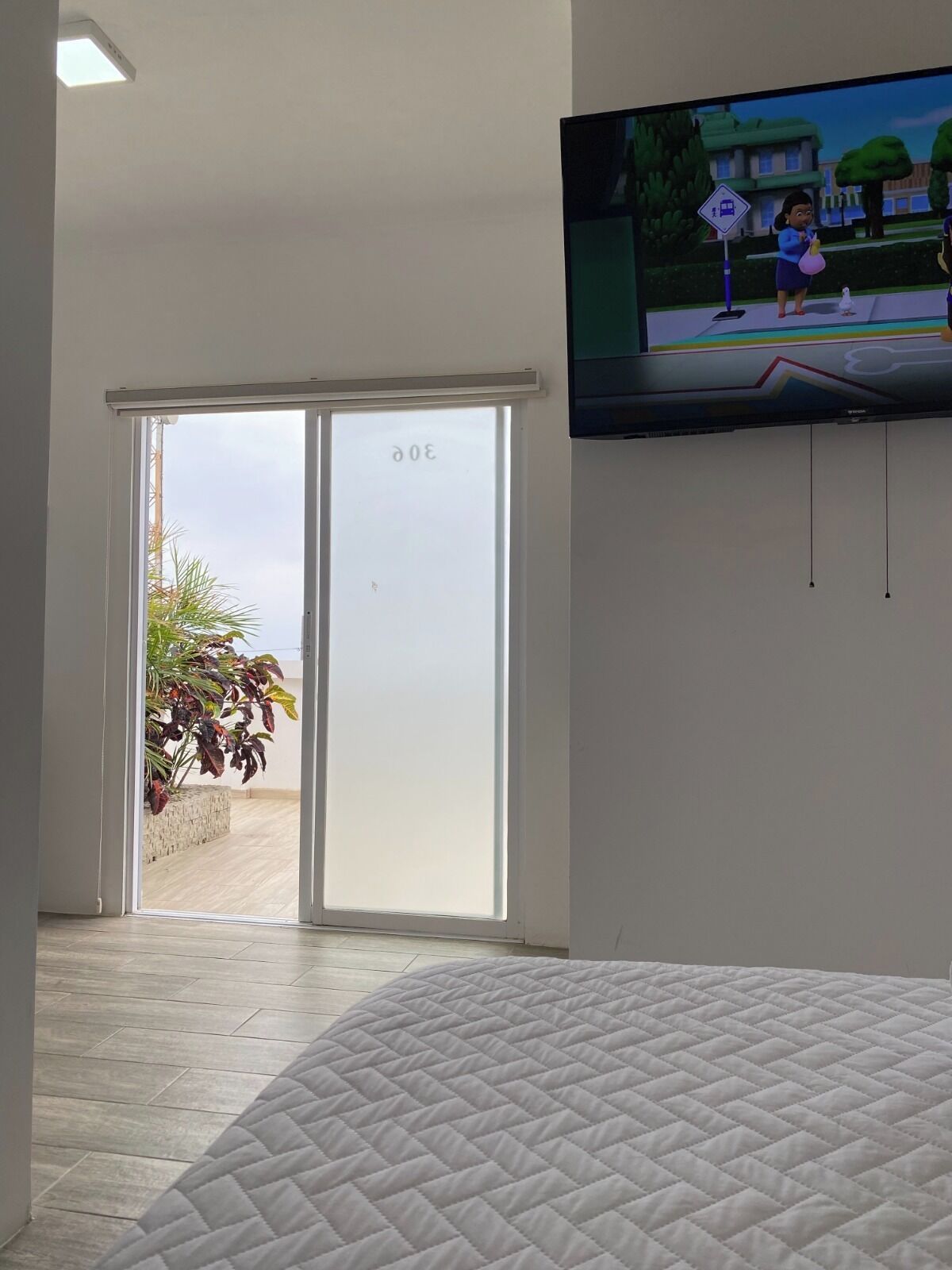 Un dormitorio con cama, puerta corrediza de vidrio que da a un espacio exterior y televisor montado en la pared.