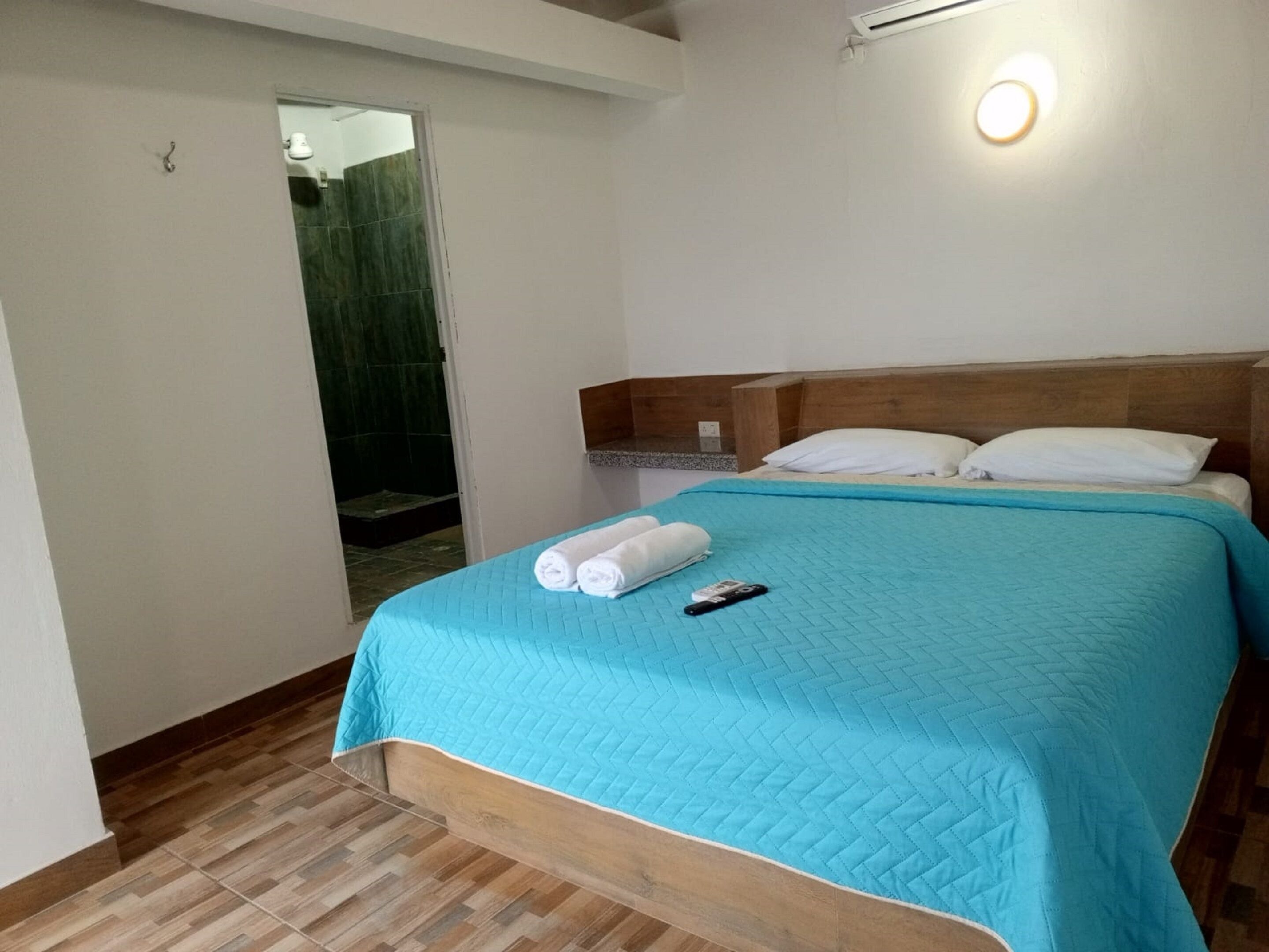 A hotel room with a wooden headboard, a blue quilted bedspread, two white pillows, and a remote control on the bed.