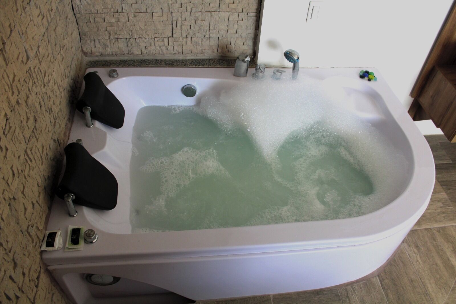 A large, rectangular hot tub with a greenish water color, surrounded by a stone wall and a wooden floor.