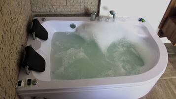 A large, rectangular hot tub with a greenish water color, surrounded by a stone wall and a wooden floor.