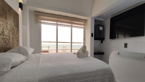 A hotel room with a large bed, a TV mounted on the wall, and a view of the sea through the window. - Terramar Hoteles  (Crucita)