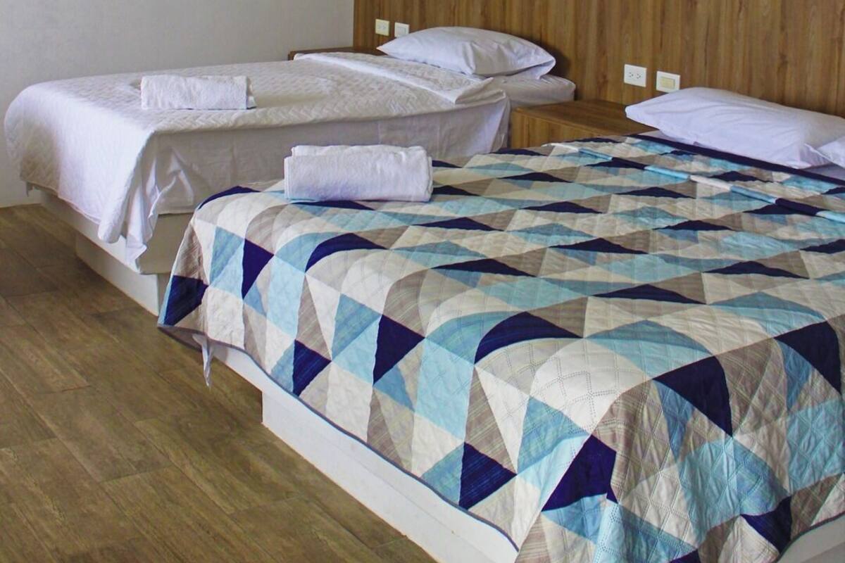 A hotel room with two beds, a wooden headboard, and a painting of a sunset over water on the wall.