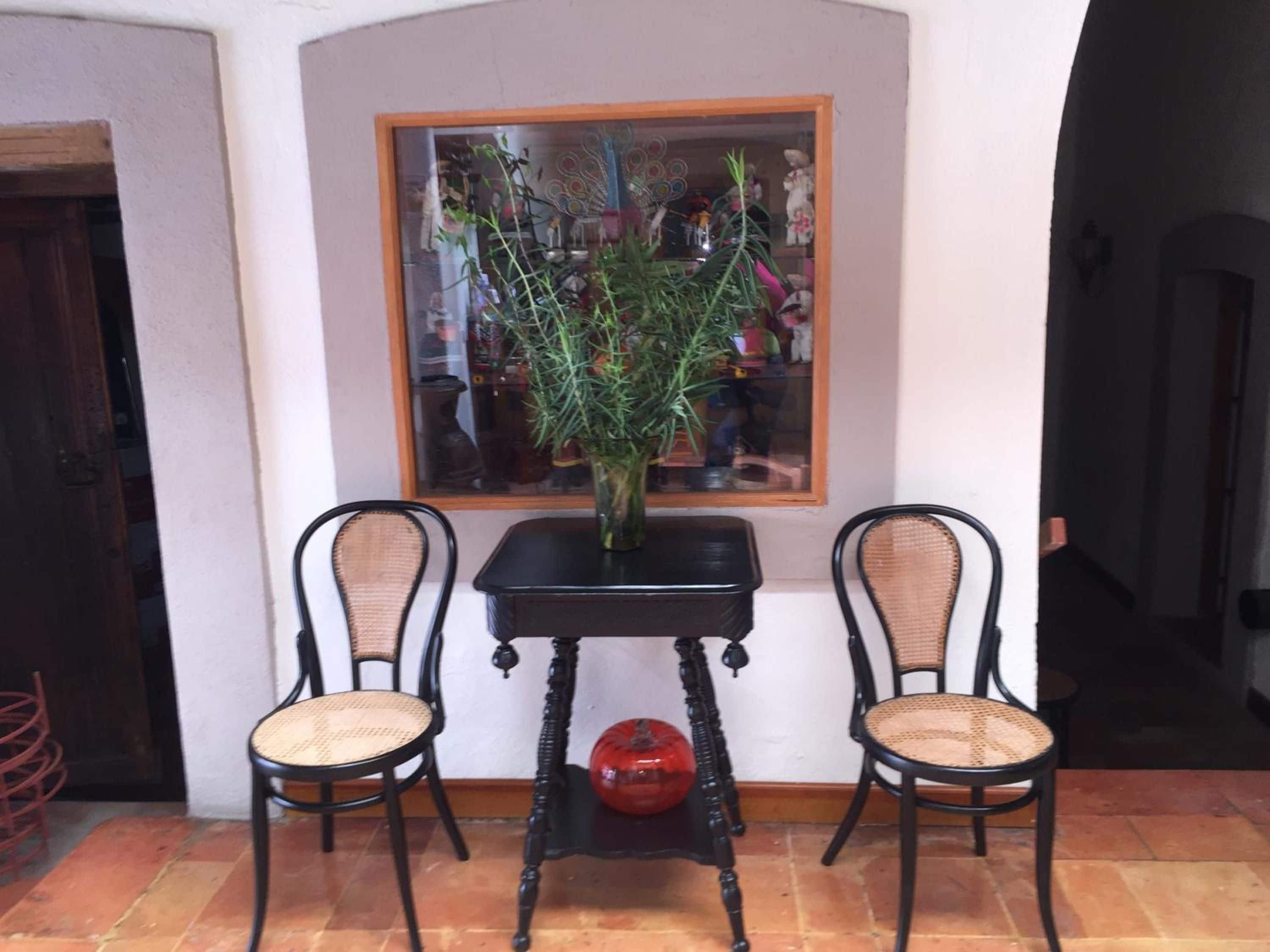 Una habitación con dos sillas de mimbre, una mesa negra y una planta en maceta.