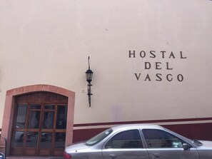 A building with a sign reading "HOSTAL DEL VASCO" and a car parked in front.