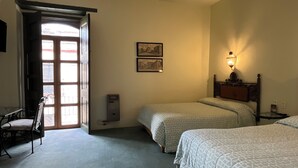 A hotel room with two beds, a chair, a heater, a wall-mounted lamp, and a door leading outside. - Casa del Pingorongo (Zacatecas)