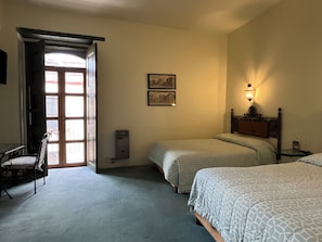 A hotel room with two beds, a chair, a heater, a wall-mounted lamp, and a door leading outside. - Casa del Pingorongo (Zacatecas)