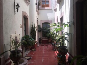 A narrow alley with red-tiled flooring, potted plants, and traditional lanterns.