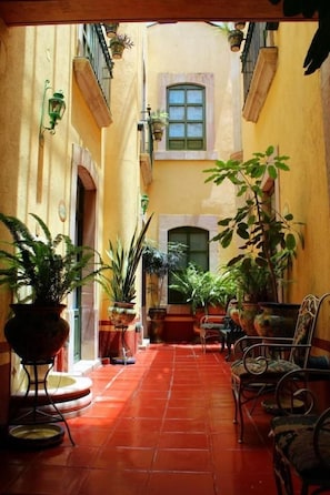 Un patio estrecho con suelo de baldosas, plantas en macetas y mobiliario exterior.