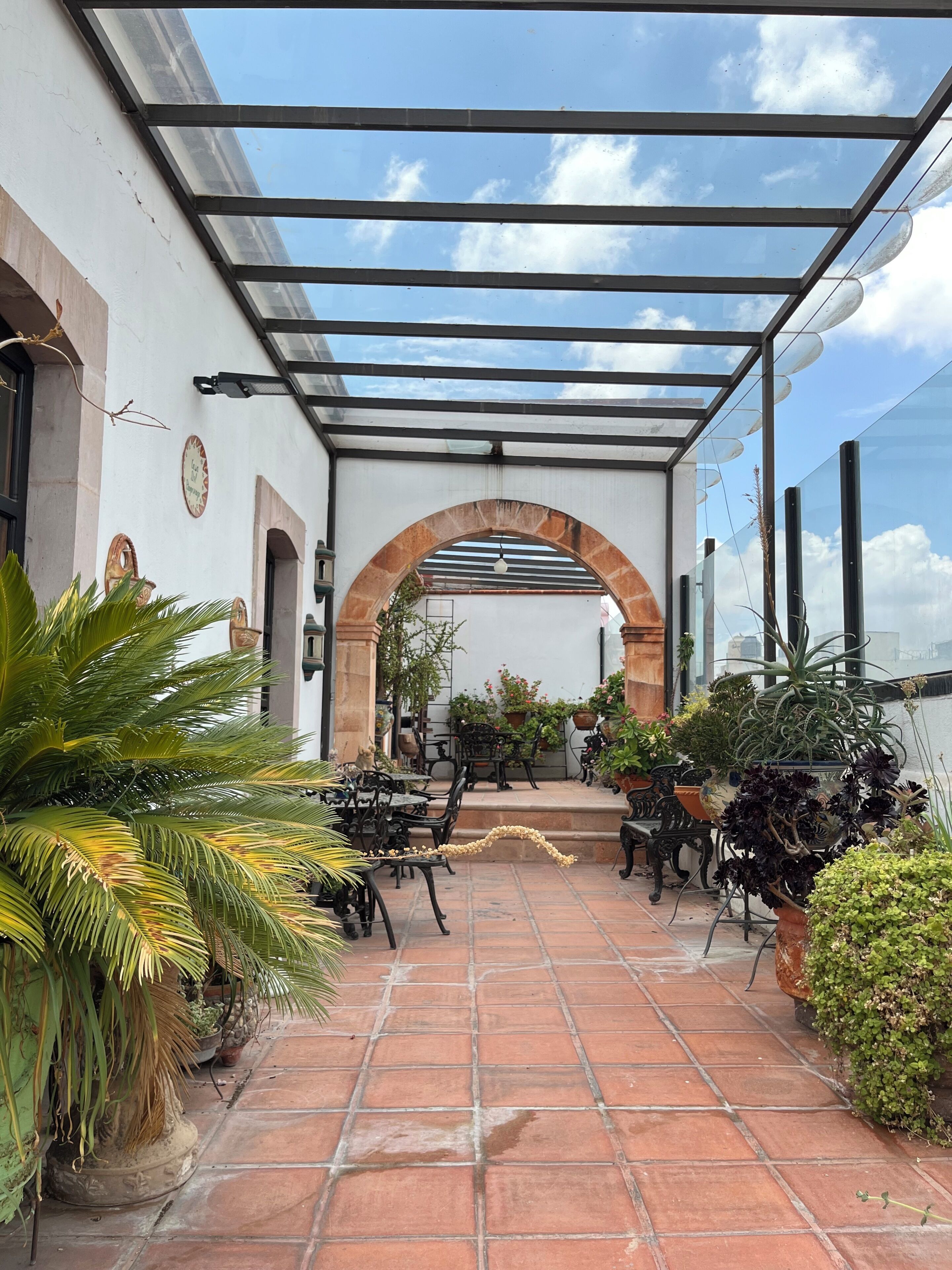 Un patio al aire libre con pérgola, suelo de baldosas y plantas en macetas.