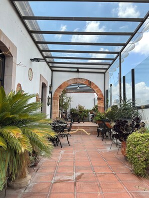 Un patio al aire libre con pérgola, suelo de baldosas y plantas en macetas.