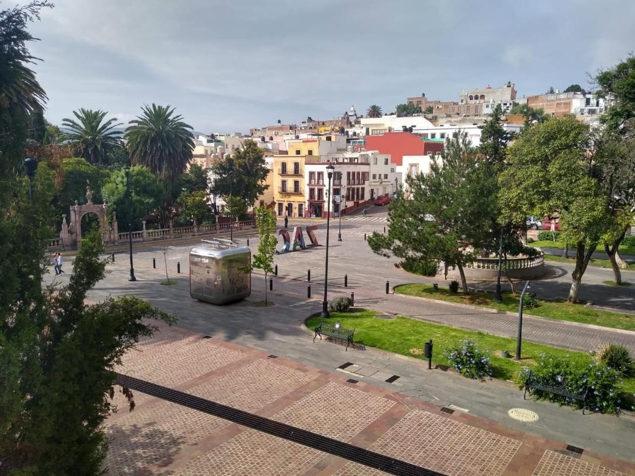 Una plaza con un monumento central, edificios circundantes y una zona verde.
