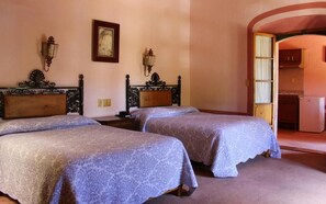 Una habitación con dos camas, cada una con cabecero y mesita de noche. Hay un cuadro en la pared y una lámpara también en la pared.