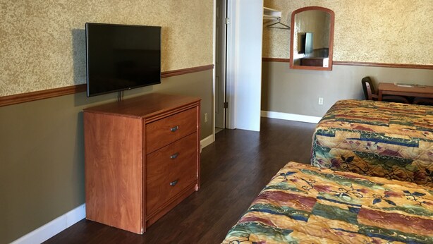 A hotel room with a wooden dresser, a flat-screen TV, a bed with a colorful quilt, a wooden desk, and a mirror on the wall. - Budget Inn (Jefferson City)