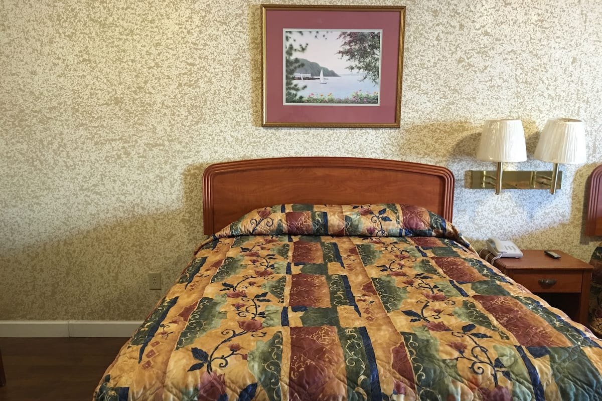 A neatly made bed with a floral quilt, a framed picture on the wall, and a bedside lamp.