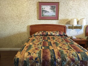 A neatly made bed with a floral quilt, a framed picture on the wall, and a bedside lamp. - Budget Inn (Jefferson City)
