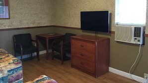 A small room with a wooden desk, two chairs, a television on a stand, and an air conditioning unit. - Budget Inn (Jefferson City)
