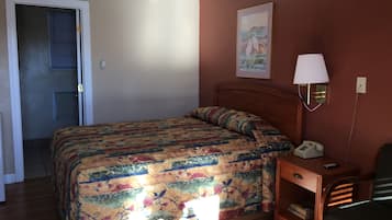 A bedroom with a bed, a nightstand with a lamp, a chair, and a painting on the wall.