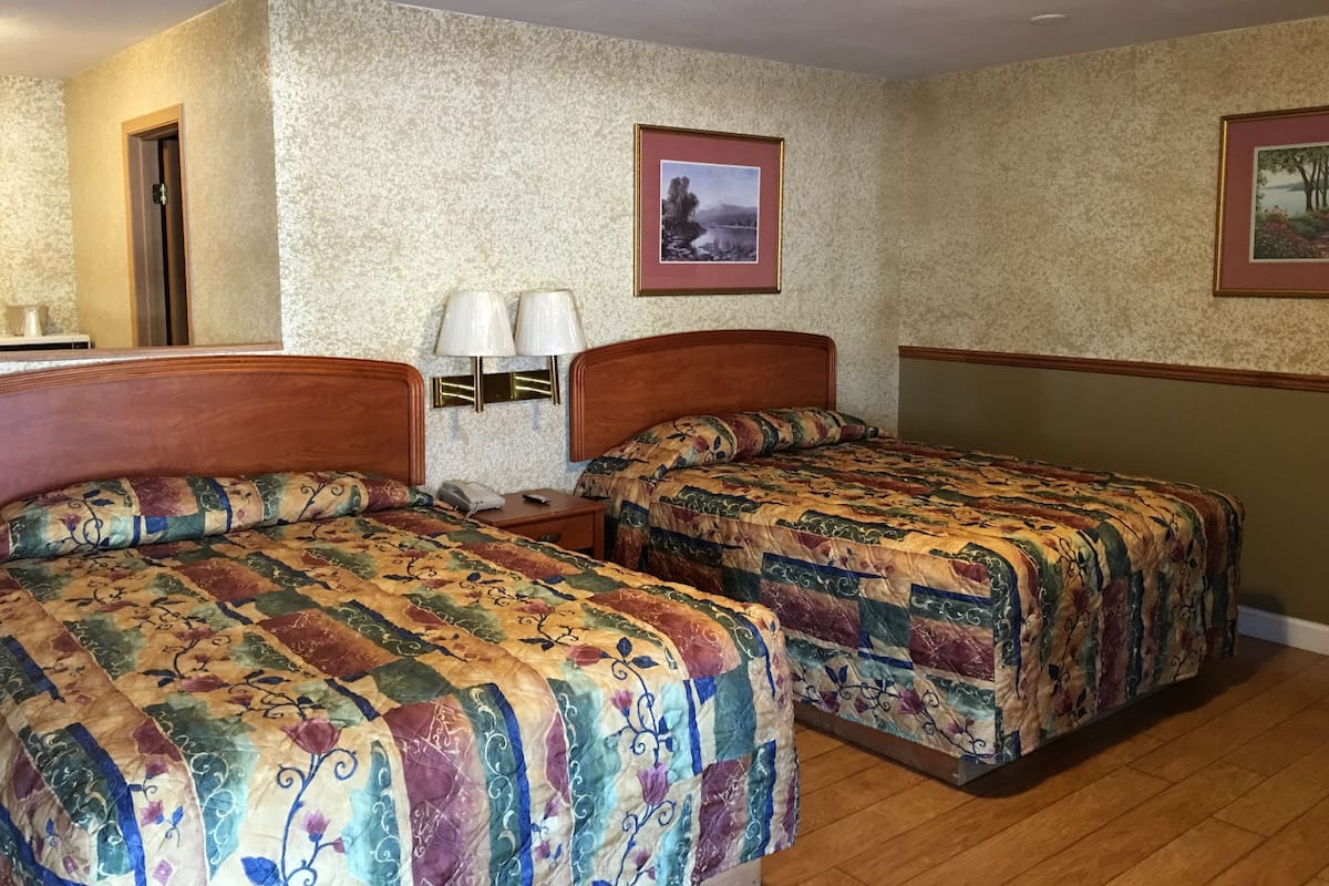 A hotel room with two beds, a nightstand, a lamp, and two framed pictures on the wall.