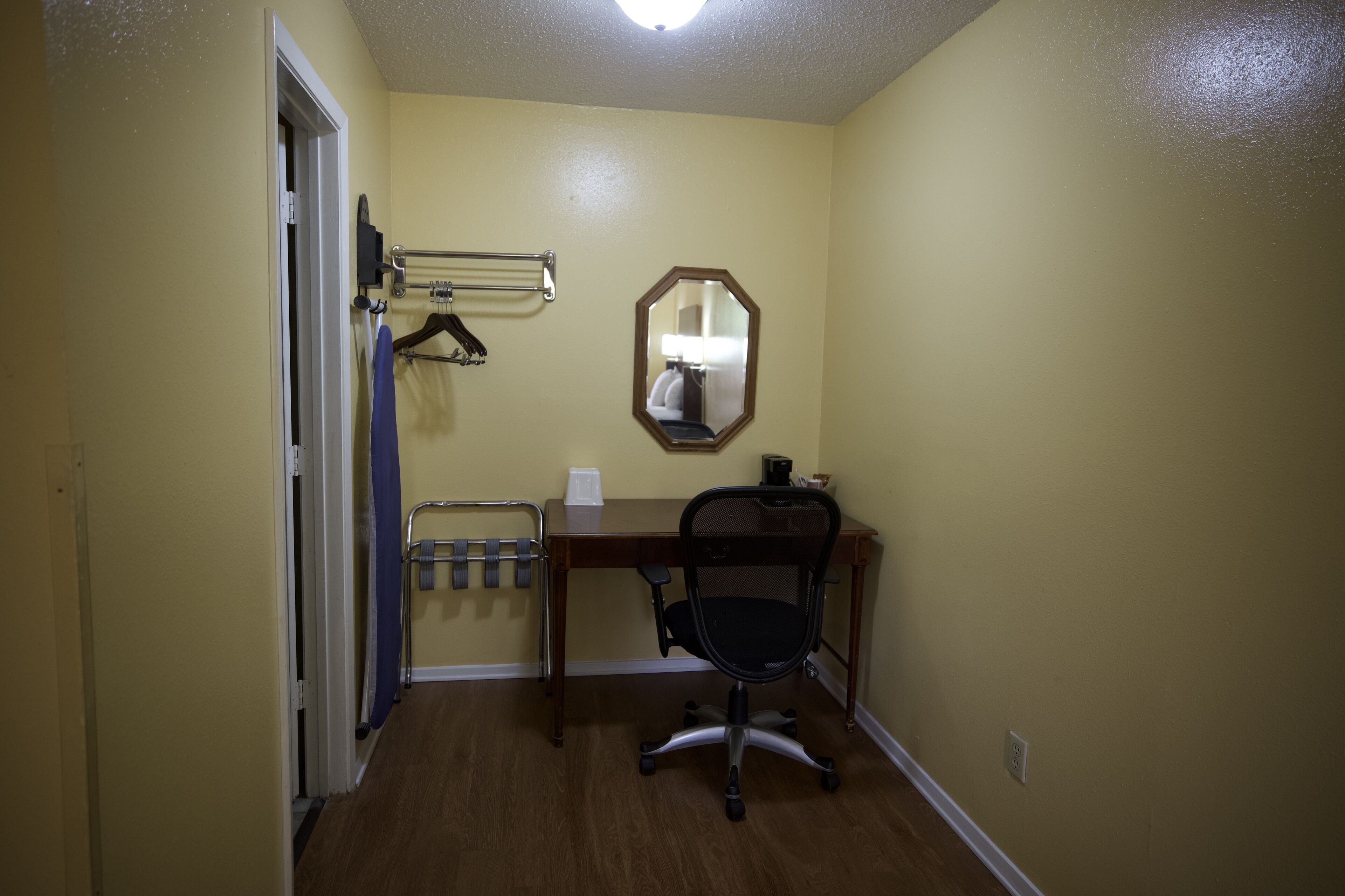A small room with a wooden desk, a chair, a mirror, and a towel rack.