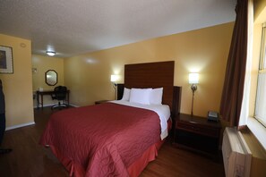 A hotel room with a large bed, two bedside lamps, a desk with a chair, and a window with curtains.