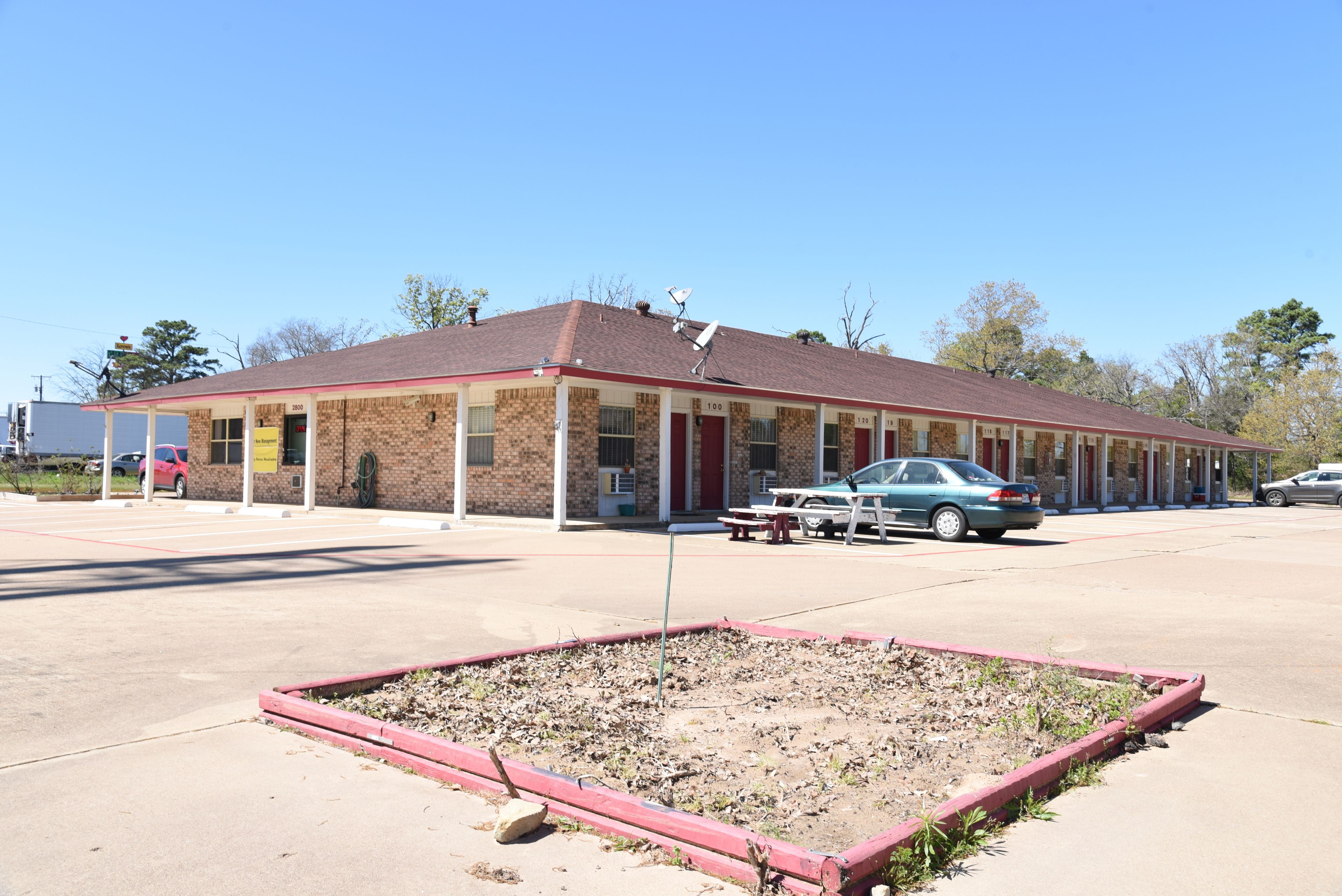 A motel with a brick facade, a red roof, and a parking lot with cars.