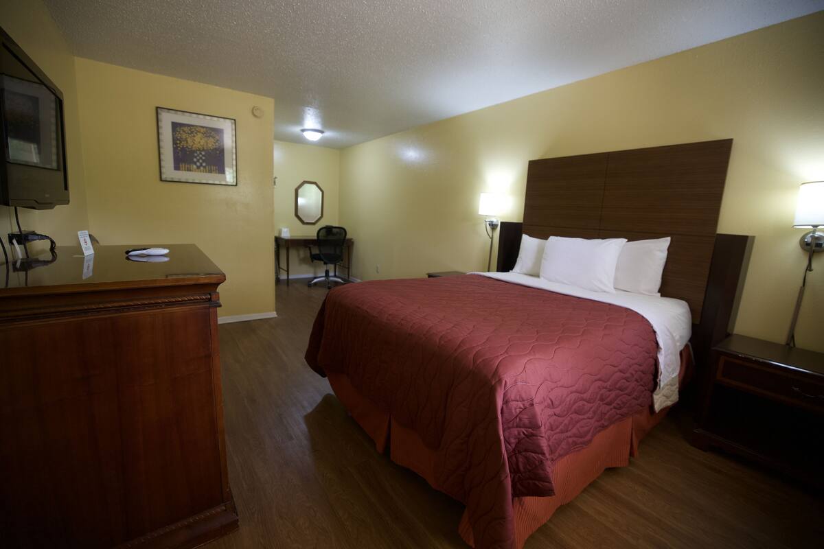 Ein Hotelzimmer mit einem hölzernen Bett, einem Schreibtisch mit Telefon, einem Sessel und einer Schreibtischlampe.