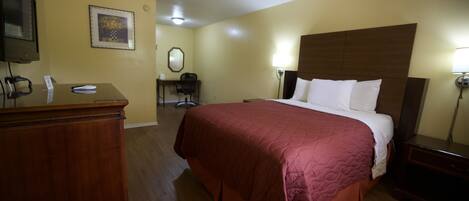 A hotel room with a wooden bed, a desk with a telephone, a chair, and a desk lamp.