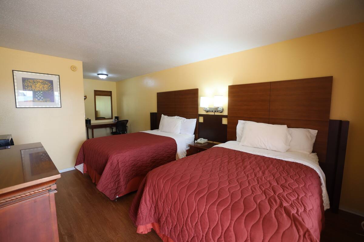 Ein Hotelzimmer mit zwei Betten, Holz-Kopfteilen, einem Schreibtisch und einem Spiegel.