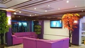 A reception area with a purple seating arrangement, a television mounted on the wall, and a large potted plant. - Merlin Grand Hotel Hat Yai (Hat Yai)