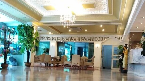 A spacious lobby with a high ceiling, ornate ceiling design, and a chandelier. There are several potted plants and a reception desk with a person standing behind it. - Merlin Grand Hotel Hat Yai (Hat Yai)