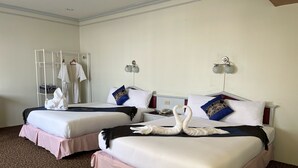 A hotel room with two beds, each with a white bedspread and pink skirts. There are two wall-mounted lamps and a mirror above the beds. - Merlin Grand Hotel Hat Yai (Hat Yai)
