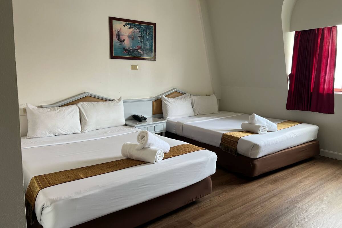 Hotellihuone, jossa on kaksi erillistä sänkyä, seinällä taulu, yöpöydällä puhelin ja ikkunassa punaiset verhot.