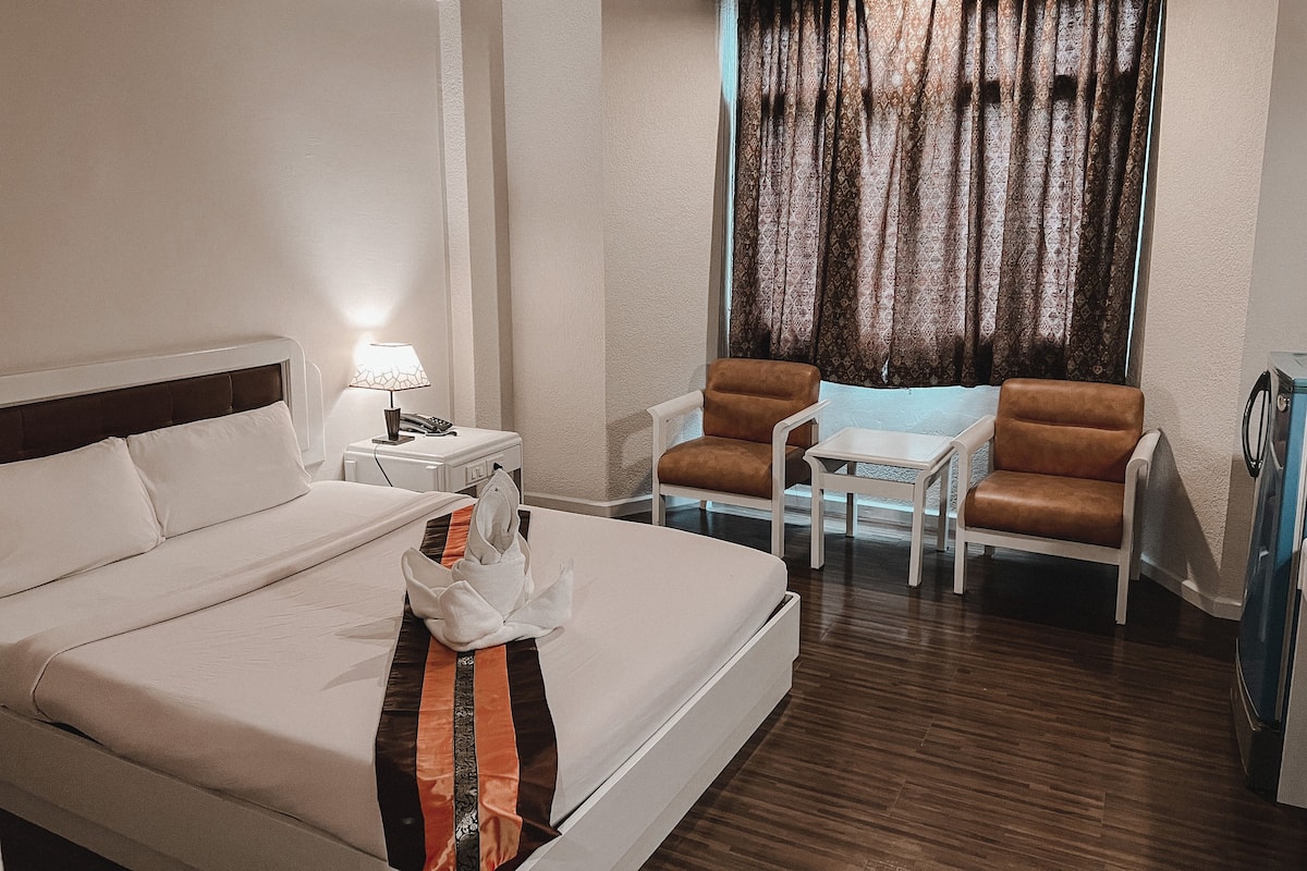 Ein Hotelzimmer mit einem Bett, einem Schreibtisch mit Lampe, zwei Stühlen, einem kleinen Tisch und einem Fenster mit Vorhängen.