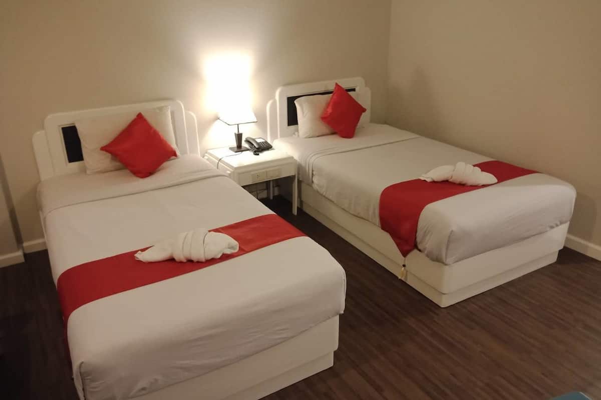 Ein Hotelzimmer mit zwei Einzelbetten, jeweils mit weißer Bettwäsche und roten Kissen. Ein Nachttisch mit Lampe und Telefon ist vorhanden.