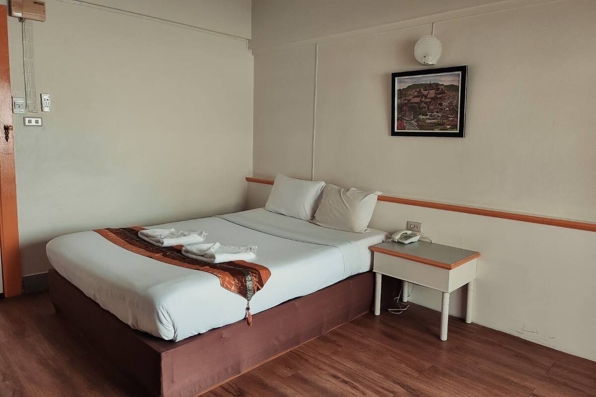 Ein Hotelzimmer mit einem Einzelbett, einem Nachttisch mit Telefon, einer Wandlampe und einem gerahmten Bild an der Wand.