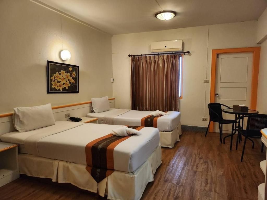 A hotel room with two beds, a desk, a chair, a picture on the wall, and an air conditioning unit.