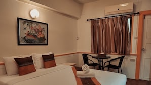 A hotel room with a bed, two pillows, a table with chairs, a window with curtains, and a wall-mounted air conditioner. - Asia Grand Hotel Hat Yai (Hat Yai)